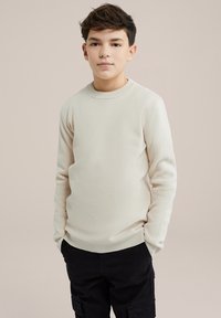 Pullover bej deschis, cu textură striată, guler rotund și mâneci lungi, asortat cu pantaloni cargo negri. Textura este moale și netedă.