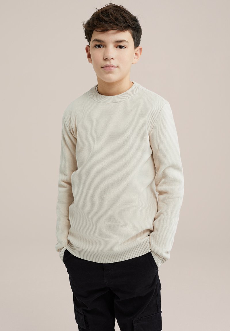 Pullover bej deschis, cu textură striată, guler rotund și mâneci lungi, asortat cu pantaloni cargo negri. Textura este moale și netedă.