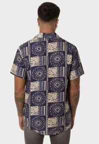 Camisa de manga corta en azul marino con un patrón geométrico, que presenta motivos circulares y florales en color crema. Fabricada con tejido ligero y de corte relajado.