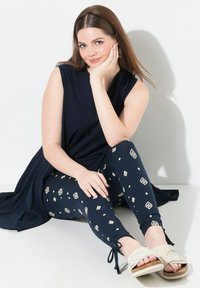 Granatowa tunika z krótkim rękawem połączona z wzorzystymi legginsami w romby w kolorze kremowym. Beżowe sandały dopełniają całość.