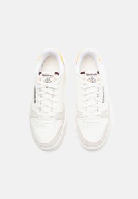 Sapatilhas brancas em couro com detalhes em camurça bege, caixa do dedo perfurada e atacadores brancos. Apresenta detalhes amarelos na língua e no logotipo.