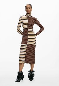 Gestreiftes Midi-Kleid in Braun, Beige und Schwarz; geripptes Material; hoher Ausschnitt; figurbetont mit gewelltem Saum; kombiniert mit schwarzen skulpturalen Stiefeln.