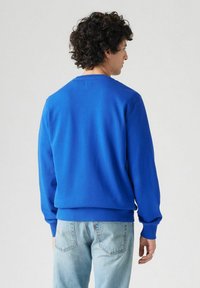 Blauwe katoenen sweatshirt met lange mouwen en geribde manchetten, met een eenvoudig ontwerp en een rechte zoom, gedragen met lichtblauwe spijkerbroek.