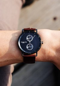 Montre avec bracelet en cuir marron, dotée d'un cadran noir, comprenant deux sous-cadrans, des aiguilles argentées et la marque "Victoria-Hyde" en texte blanc.
