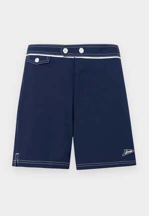 Tumši zili peldbikses ar baltiem pogu akcentiem, baltām kontrastējošām šuvēm, mazu priekšējo kabatu ar pogas atloku un Speedo logo malā.