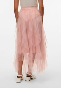 Gonna a strati di tulle rosa con orlo irregolare, caratterizzata da bordi arricciati e una cintura liscia, abbinata a scarpe con tacco quadrato di colore chiaro.