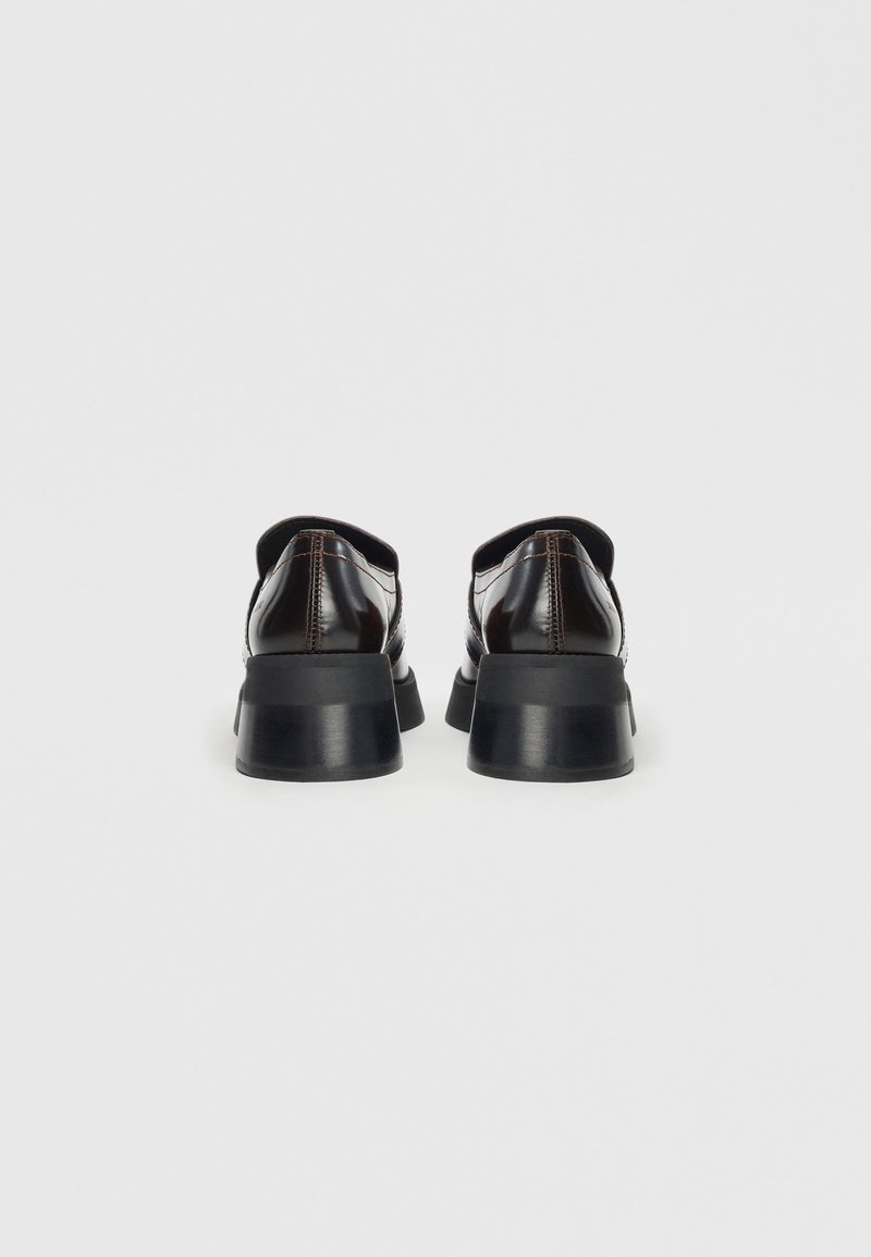 Chaussures en cuir verni noir avec un talon épais noir, présentant un bout arrondi et des coutures contrastantes le long des coutures. Texture lisse.