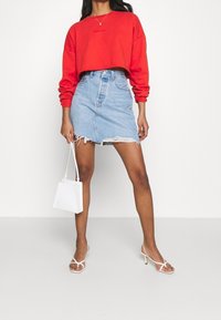 Sweatshirt rouge cropped avec un logo, associé à une mini-jupe en denim bleu clair avec un ourlet effiloché, et accessoirisé avec un petit sac blanc.