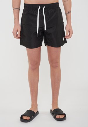 Schwarze Badehose aus einem glatten, leichten Material, mit einem elastischen Bund, weißem Kordelzug und kleinem Logodetail an der Seite.