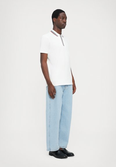 Hvit polo skjorte med stripete krage, parret med lyseblå, løstsittende jeans og svarte sko. Designet er enkelt og uformelt.