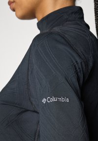 Čierny dlhý rukáv top s vysokým golierom, s textúrovanými vzormi a bielym logom "Columbia" na ľavom rukáve.