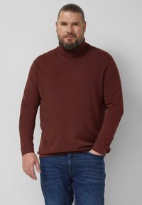 Brązowy sweter z golfem z miękkiego materiału z długimi rękawami, zaprojektowany z prążkowanym kołnierzem i mankietami, w połączeniu z niebieskimi dżinsami.