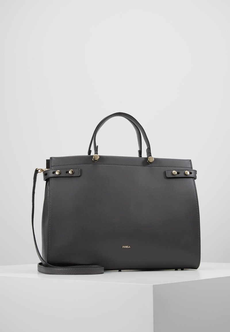 Musta Furla-nahkalaukku, jossa on yläkahvat, irrotettava olkahihna sekä kultaiset niitti- ja logoyksityiskohdat valkoisella pinnalla.