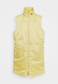 Gul ärmlös väst, glänsande tyg, hög krage, dragkedja fram, två sidofickor och liten logotypdetalj vid halsringningen.