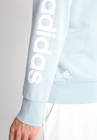 Sweatshirt bleu clair avec logo "adidas" blanc sur la manche et petit logo à l'avant. Tissu doux avec poignets et ourlet côtelés.