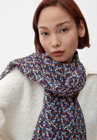 Écharpe à motifs dans des nuances de bleu, rouge, jaune et blanc. Tissu léger avec une texture douce, drapée autour du cou contre un pull crème.