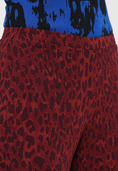 Rote Leggings mit Leopardenmuster, aus glattem Material und hoher Taille, mit taillierter Passform und subtiler glänzender Oberfläche.