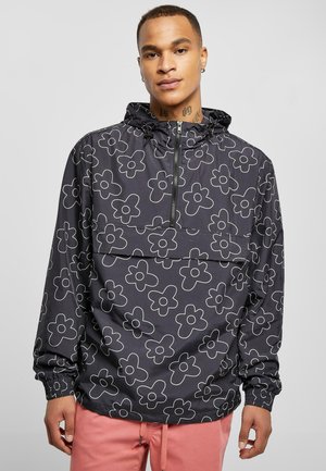 Chaqueta de sudadera negra con un diseño floral contorneado, cierre frontal de media cremallera y capucha ajustable, con un bolsillo en el pecho, fabricada en una tela ligera.