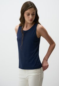 Top senza maniche blu navy in tessuto liscio, con scollatura rotonda e design aderente, abbinato a pantaloni bianchi. Senza motivi visibili.
