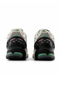 New Balance sneakers featuring a cream upper, black accents, green details, and a textured mesh design for breathability.