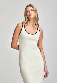 Ribbed, fitted dress in off-white with black trim on the neckline. Sleeveless design with a streamlined silhouette and soft texture.
