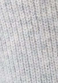 Hellgrauer Strickstoff mit einer weichen, strukturierten Oberfläche. Verfügt über ein Rippenmuster und subtile Variationen in der Fadendicke.