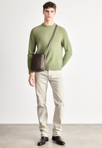 Zöld gyapjúpulóver, világos bézs színű pamut farmer, barna bőr válltáska, sötétbarna bőr csizma, letisztult dizájn, semleges háttér.