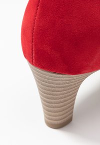  chaussure haute en daim rouge avec un talon beige strié. La chaussure a une texture lisse et une forme arrondie, mettant en valeur son design épuré.
