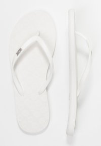 Vita flip-flops med en texturerad fotbädd och vita gummiremmar. Har en liten logotyp på en rem. Platt sula och släta kanter.