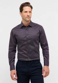 Maglietta a maniche lunghe di colore viola scuro con una trama a motivo, caratterizzata da pois bianchi e rossi, e colletto standard con chiusura a bottoni.