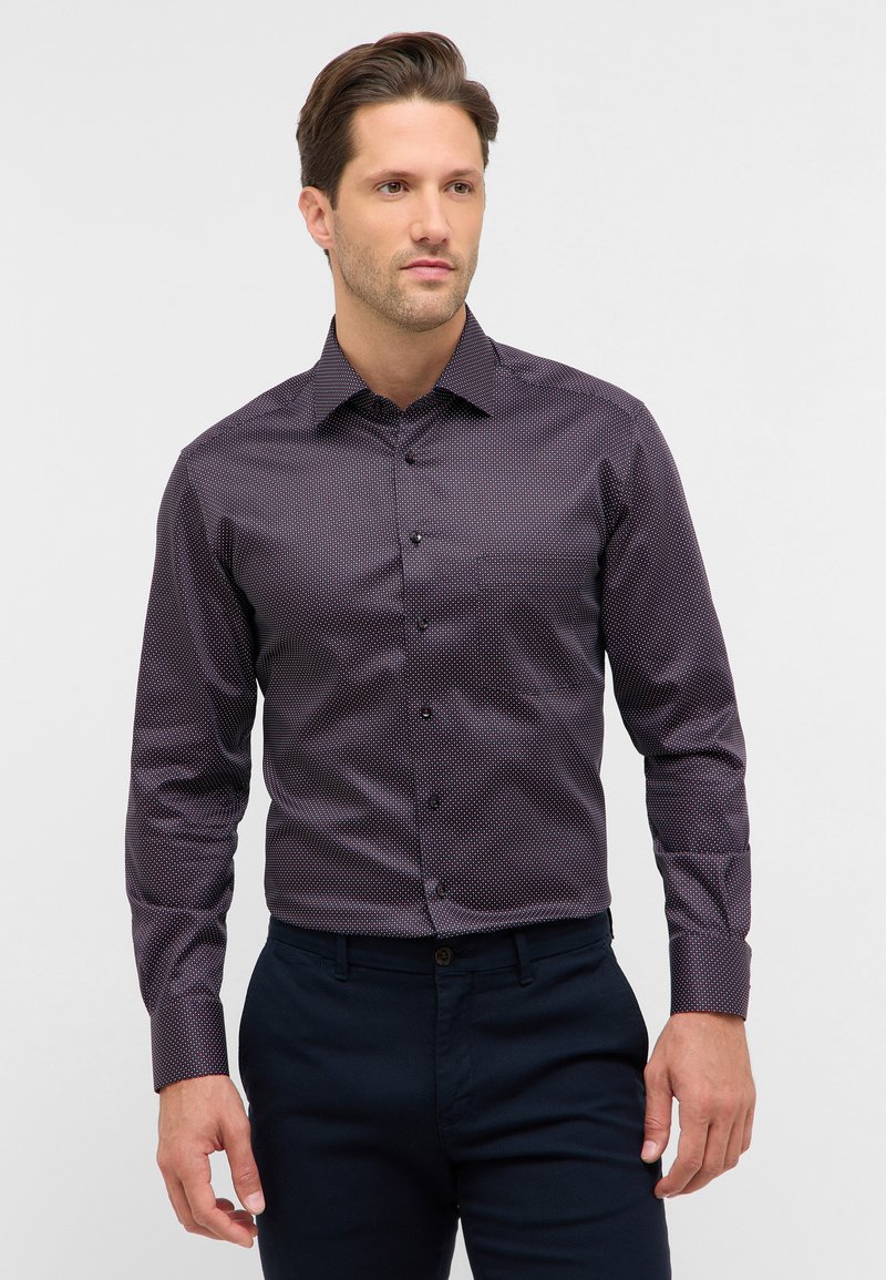 Maglietta a maniche lunghe di colore viola scuro con una trama a motivo, caratterizzata da pois bianchi e rossi, e colletto standard con chiusura a bottoni.