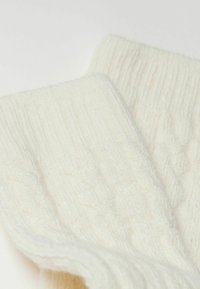 Sweter w kolorze kremowym o splocie warkoczowym, z grubą teksturą prążkowaną i miękkim, przytulnym materiałem. Ozdobiony wzorami warkoczowymi na całej powierzchni.