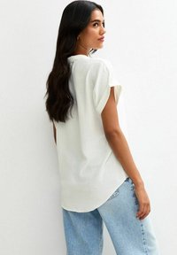 Vit, kortärmad blus med en avslappnad passform, med en texturerad tyg och rundad nederkant, i kombination med ljusblå, löst sittande jeans.