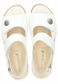Sandales en cuir blanc avec un design incurvé, bout ouvert, deux sangles ajustables et un accent décoratif en métal avec un bouton-pression. Semelle intérieure texturée.