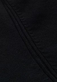 Tissu noir montrant un tricot texturé avec des coutures visibles. Le matériau semble doux et dense, mettant en avant un ton sombre et uniforme.