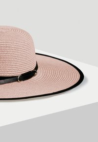 Szeroki kapelusz z różowego słomkowego materiału z czarną skórzaną opaską i srebrnymi detalami, charakteryzujący się teksturowanym splotem i kontrastowym brzegiem.