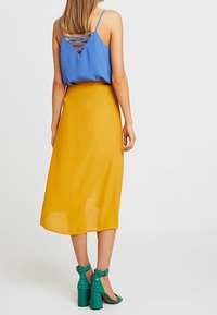 Top blu sleeveless con schiena incrociata, abbinato a una gonna midi gialla e sandali con tacco verde alla caviglia. Tessuto texturizzato.