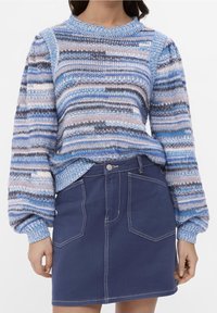 Niebiesko-szary sweter w paski z dzianiny z bufkami na rękawach; zestawiony z ciemną spódnicą z denimu z przednimi kieszeniami i kontrastowymi przeszyciami.