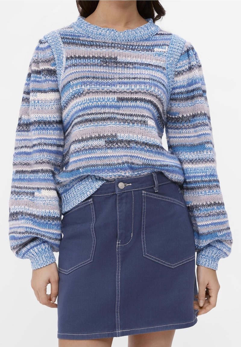 Niebiesko-szary sweter w paski z dzianiny z bufkami na rękawach; zestawiony z ciemną spódnicą z denimu z przednimi kieszeniami i kontrastowymi przeszyciami.