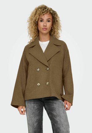 Veste marron à double boutonnage avec de grands revers et un tissu texturé, dotée de deux boutons argentés et de manches larges, assortie d'un haut blanc.
