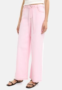 Jasnoróżowe spodnie typu wide-leg wykonane z dżinsu z elastycznym paskiem w pasie. Posiadają kontrastowe przeszycia i boczne paski. W komplecie płaskie przednie kieszenie.