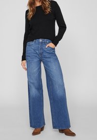 Leveälahkeiset keskisinisen farkut, korkealla vyötäröllä, haalistuneilla osioilla ja klassisella viiden taskun mallilla. Yhdistetty mustaan neuleeseen ja ruskeisiin saappaisiin.