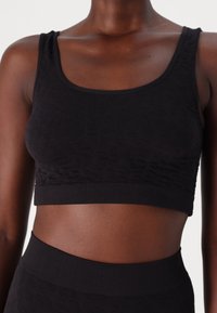 Black crop top with a textured pattern, made of a stretchy material. Features a scoop neckline and ribbed band at the bottom.