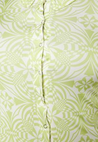 Blusa verde e branca com padrão, com frente de botão, tecido suave, apresentando formas geométricas e designs florais por todo o lado.