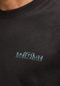 Μαύρο t-shirt με γαλάζιο κείμενο «August 5th Kraftskiva hosted by Marc O'Polo Denim» στην αριστερή πλευρά του στήθους.