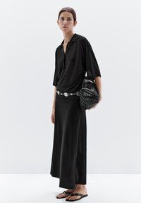 Black short-sleeve shirt with a pocket, paired with a long black skirt. Accessorized with a woven black bag and flat black sandals.