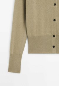 Cardigan beige à manches longues avec boutons noirs, poignets et ceinture côtelés sur fond blanc, montrant la manche gauche et le bas devant.