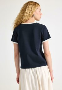 Navy T-shirt met korte mouwen, voorzien van een contrasterende lichte rand bij de halslijn en de mouwranden. Soepele stoftextuur.