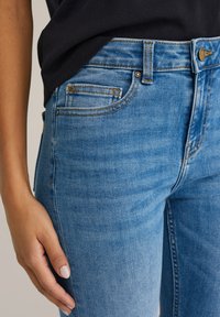 Világoskék farmernadrág testhezálló szabással. Jellemzői az öt zsebes kialakítás, a réz gomb és a kontrasztos varrás.