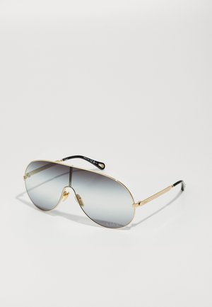 Arany aviátor napszemüveg, fokozatos szürke lencsékkel, sportos fémkerettel és fekete acetát templomvégekkel, a kereten dombornyomott márkázással.